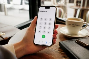 Main tenant un iPhone affichant le clavier d'appel dans un café lumineux