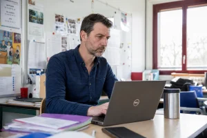 Enseignant consultant sa messagerie académique sur un ordinateur portable en salle des professeurs