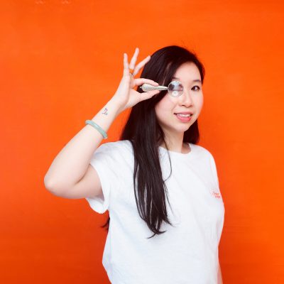 Véronique Duong qui anime le podcast Maitriser le SEO porte à son oeil une loupe, sur un fond orange